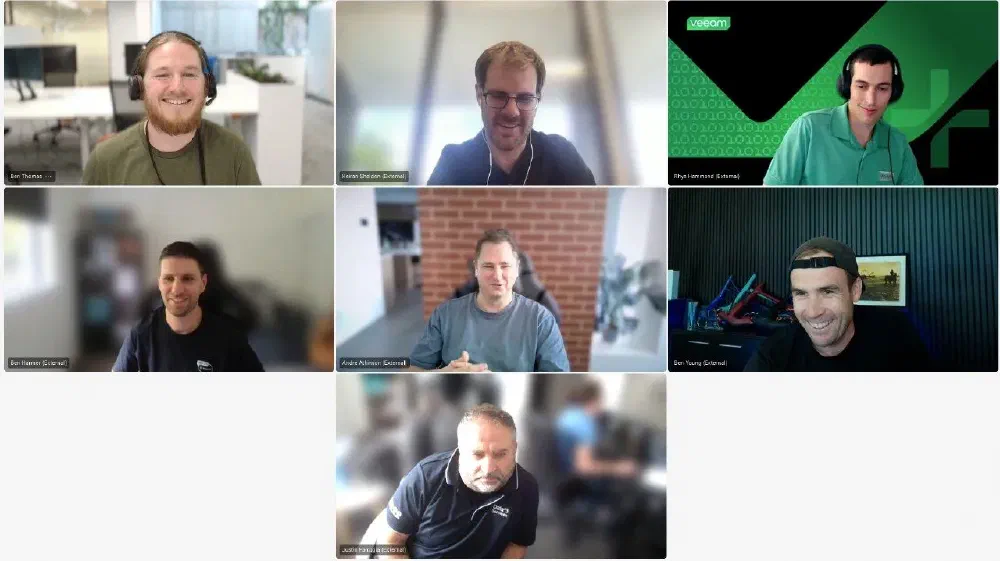 Veeam 100 ANZ team virtual meeting featuring seven participants in a video call. The team members appear engaged, with some smiling and others in discussion. The Veeam-branded background is visible in one participant&rsquo;s frame, reinforcing the team&rsquo;s affiliation. This image highlights collaboration among Veeam&rsquo;s Australia and New Zealand (ANZ) community.