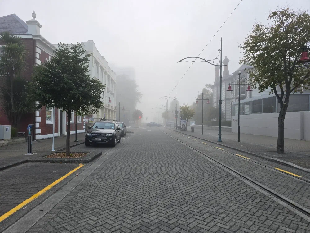 Foggy street with parked cars and tram tracks.
